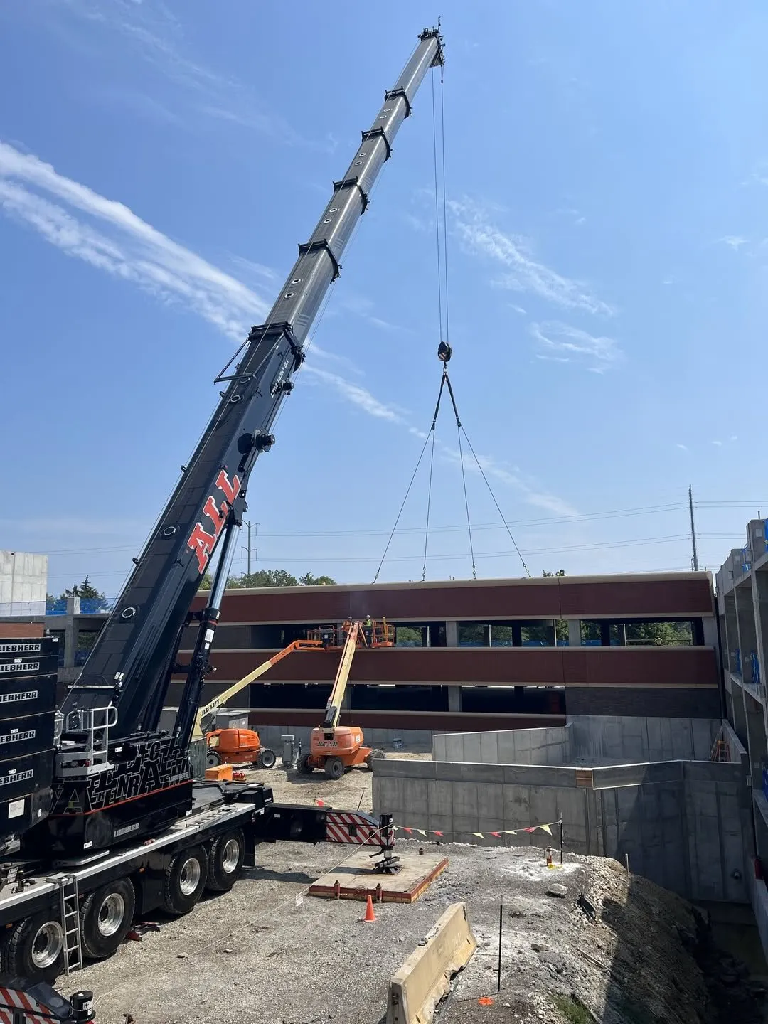 A mobile crane lifting a precast panel into place at the Lake Forest parking structure, with boom lifts positioned on the deck below