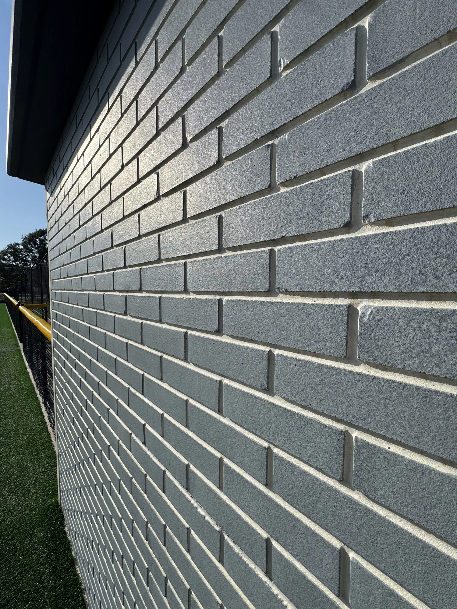 Close-up of the brick-pattern precast surface at Field 32, painted light blue, with the running bond and joint depth cast into the concrete