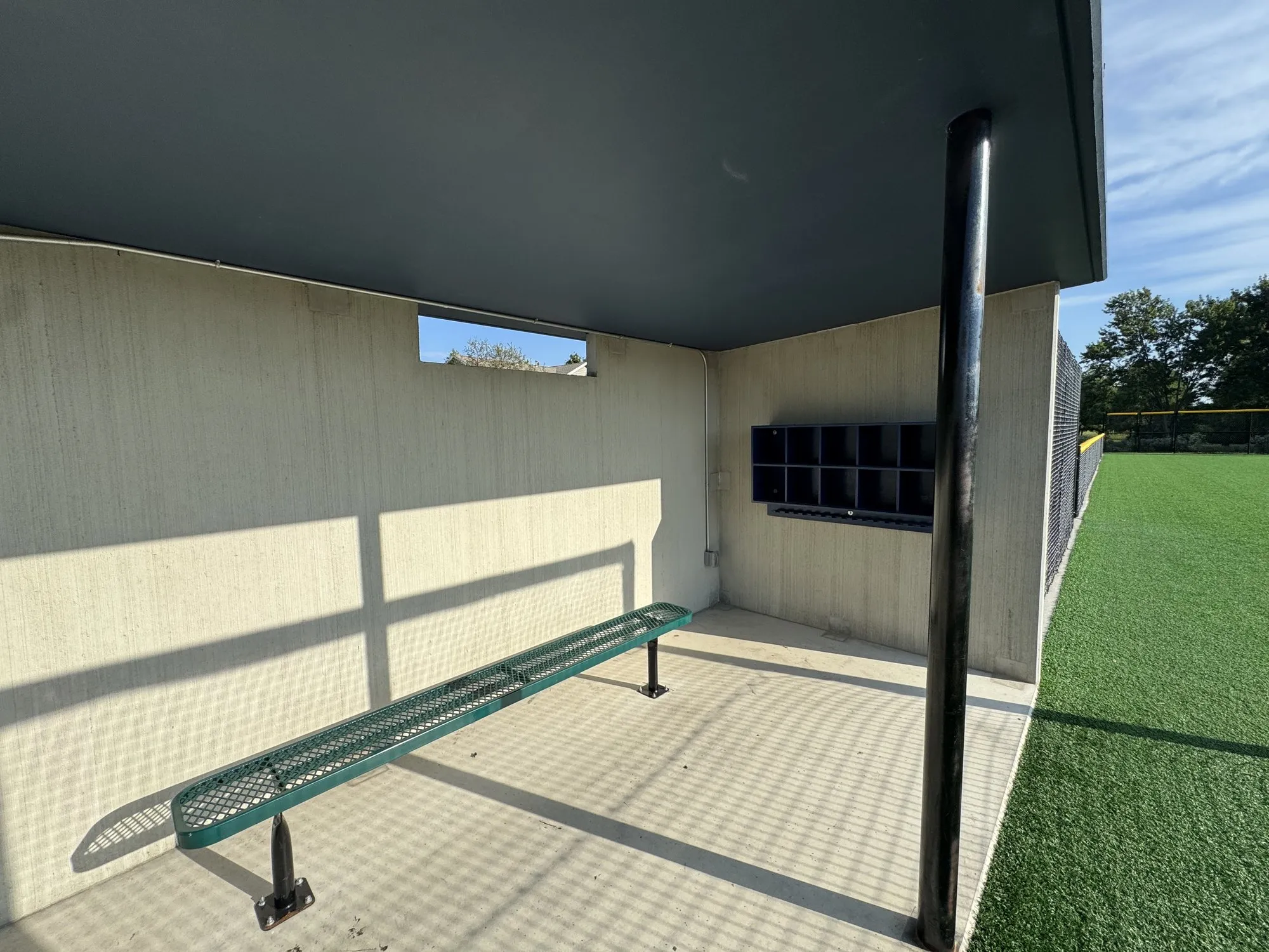 Inside a Field 32 dugout: a long bench, wall cubbies, and the deep roof overhang, all in precast concrete
