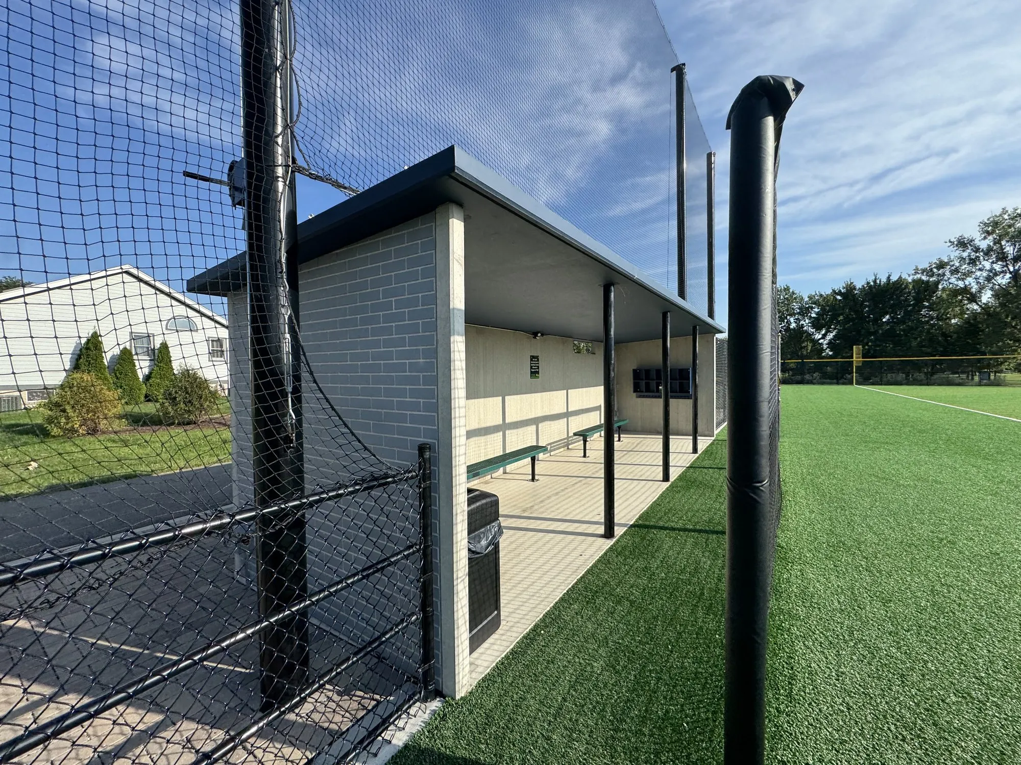 Third base dugout at Field 32, light blue brick-pattern precast with a dark flat roof, behind the fence and netting